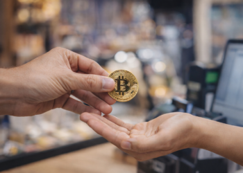 Manos intercambiando una moneda de bitcoin en un comercio, representando un pago en BTC.
