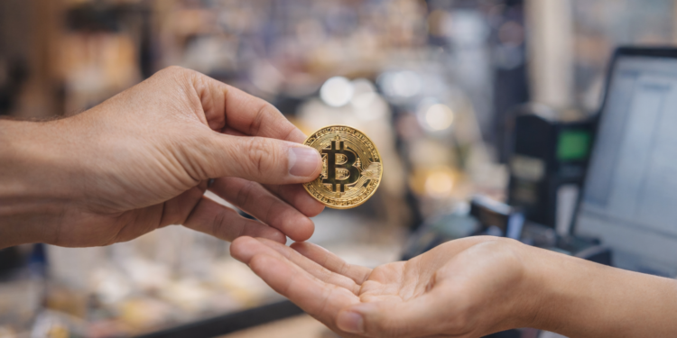 Manos intercambiando una moneda de bitcoin en un comercio, representando un pago en BTC.