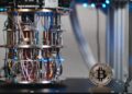 Moneda física de bitcoin dorada al lado de una computadora cuántica sobre un escritorio en un laboratorio.