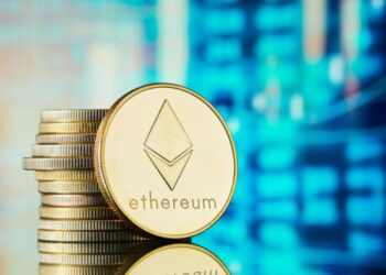 Moneda física de ETH dorada sobre un escritorio con un fondo azul.