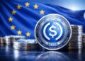 Monedas de la stablecoin USDC en primer plano con la bandera de la Uniรณn Europea desenfocada al fondo.