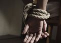 Fotografía de un par de manos maniatadas con cuerda en una silla, en simbología a un secuestro.