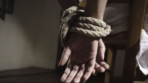Fotografía de un par de manos maniatadas con cuerda en una silla, en simbología a un secuestro.