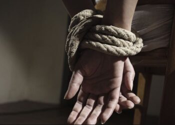 Fotografía de un par de manos maniatadas con cuerda en una silla, en simbología a un secuestro.