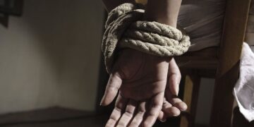 Fotografía de un par de manos maniatadas con cuerda en una silla, en simbología a un secuestro.
