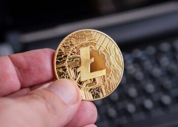 Una mano sostiene una moneda dorada de litecoin.