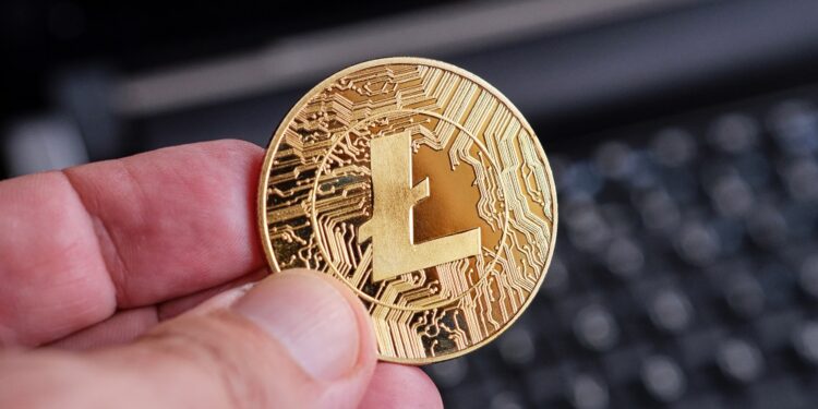 Una mano sostiene una moneda dorada de litecoin.
