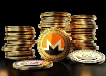Una moneda física de monero delante de pilas de monedas