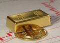 un lingote de oro sobre una moneda de bitcoin y detrás gráficos de precios rojos.