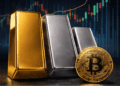Una moneda física de bitcoin junto a lingotes de oro y plata delante de un gráfico de precios.