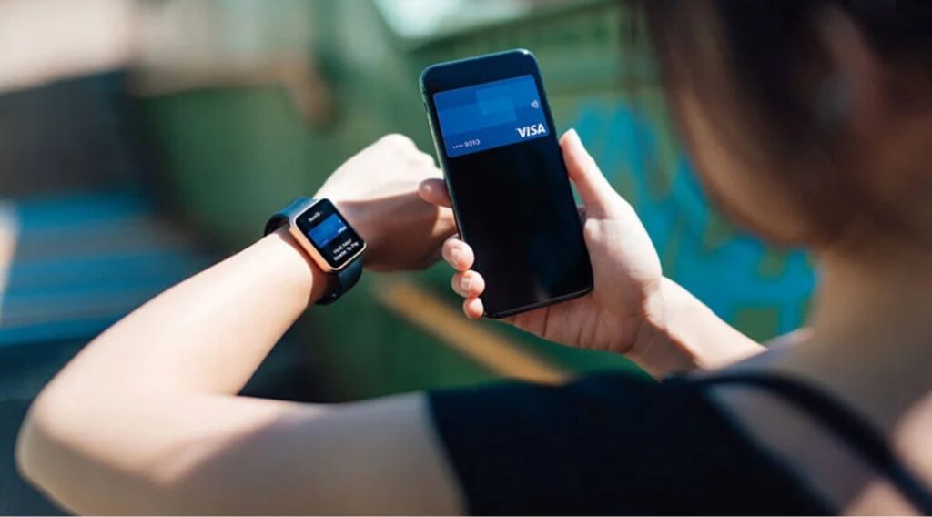 Persona usando un smartwatch y un smartphone para realizar un pago contactless con una tarjeta Visa digitalizada.