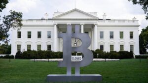 Logo de Bitcoin frente a la Casa Blanca, esta última tiene un letrero que dice "Closed (cerrado)".