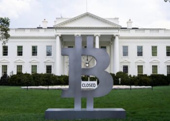 Logo de Bitcoin frente a la Casa Blanca, esta última tiene un letrero que dice "Closed (cerrado)".