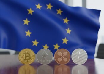 Bandera de la Unión Europea con distintas criptomonedas sobre un escritorio.