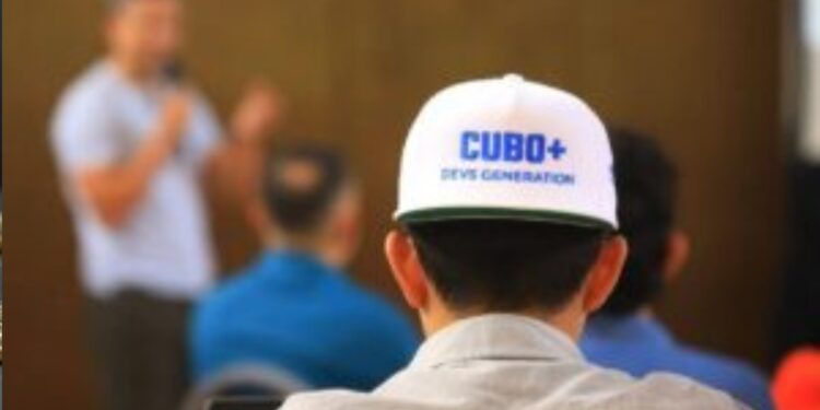 Fotografía de un estudiante de CUBO+ usando una gorra con el logo del programa educativo mientras ve clases.