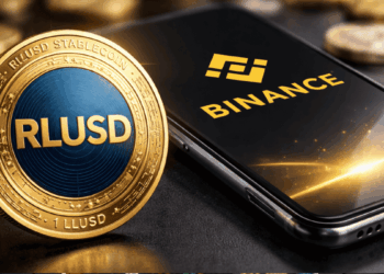 Una moneda de RLUSD junto a un celular que muestra el logo de Binance.