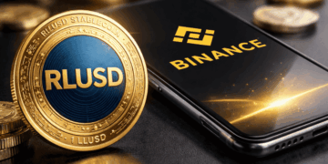 Una moneda de RLUSD junto a un celular que muestra el logo de Binance.