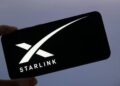 Mano sujetando un teléfono inteligente que refleja el logo de Starlink.