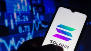 Una mano sujetando un teléfono inteligente que muestra el logo de Solana, y de fondo una pared de gráficas en color azul.