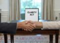 Par de manos estrechándose en una oficina de la Casa Blanca, con un documento que dice "Clarity Act" en el fondo.