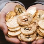 Dos manos sotienen un grupo de bitcoins físicos.