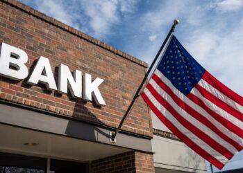Edificio de ladrillos con un cartel que dice BANK, con la bandera de EE. UU. izada.