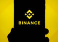 Mano sujetando un teléfono que refleja el logo de Binance.