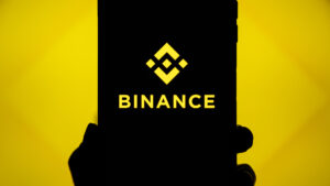Mano sujetando un telรฉfono que refleja el logo de Binance.