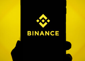 Mano sujetando un teléfono que refleja el logo de Binance.