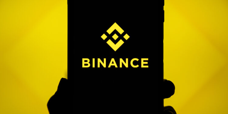Mano sujetando un teléfono que refleja el logo de Binance.