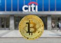 Una moneda fรญsica de Bitcoin dorada en primer plano con el logotipo de un banco Citi desenfocado al fondo