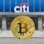 Una moneda fรญsica de Bitcoin dorada en primer plano con el logotipo de un banco Citi desenfocado al fondo
