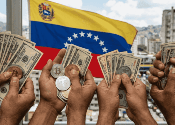 varias manos sosteniendo billetes de dólar norteamericano y monedas de bitcoin y USDT frente a una bandera de Venezuela.