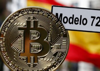 Moneda física de bitcoin dorada con un cartel que dice "Modelo 721" y la bandera de España detrás.