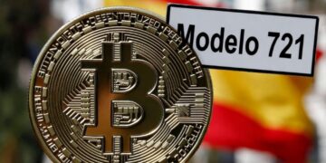 Moneda física de bitcoin dorada con un cartel que dice "Modelo 721" y la bandera de España detrás.
