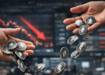 Manos dejando caer monedas físicas de Ethereum frente a una pantalla bursátil con gráfico rojo en caída.
