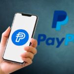 Smartphone mostrando el logo de PayPal PYUSD stablecoin con fondo azul.