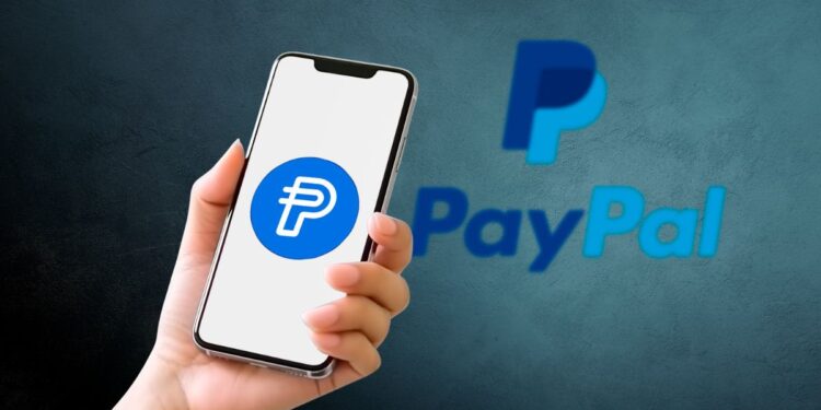 Smartphone mostrando el logo de PayPal PYUSD stablecoin con fondo azul.