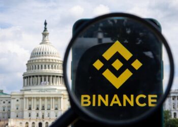 Fotografía del Senado de EE. UU. con un teléfono que muestra el logo de Binance, con una lupa sobre el logo.