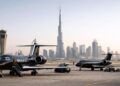 Tres jets privados de vuelos chárter estacionados en la pista con el horizonte urbano de Dubai al fondo.