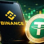 Un celular con el logo de Binance junto a una moneda física de USDT, la stablecoin de Tether.
