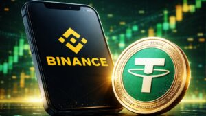 Un celular con el logo de Binance junto a una moneda física de USDT, la stablecoin de Tether.