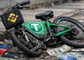 Una bicicleta con simbología de USDT paralizada, con el logo de Binance al frente, tarjetas bancarias y dólares alrededor.