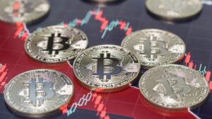 Monedas físicas de bitcoin sobre gráfico bursátil rojo de tendencia bajista.