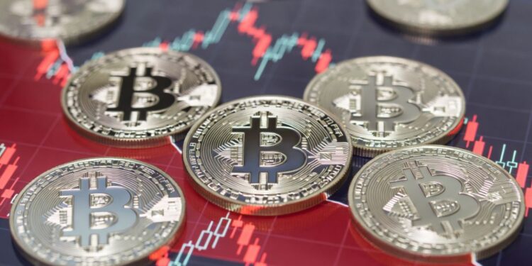 Monedas físicas de bitcoin sobre gráfico bursátil rojo de tendencia bajista.