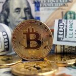 Moneda física de bitcoin dorada rodeada de billetes de 100 dólares estadounidenses.