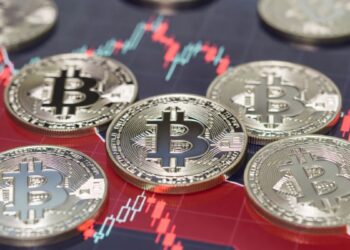 Monedas físicas de bitcoin sobre gráfico bursátil rojo de tendencia bajista.