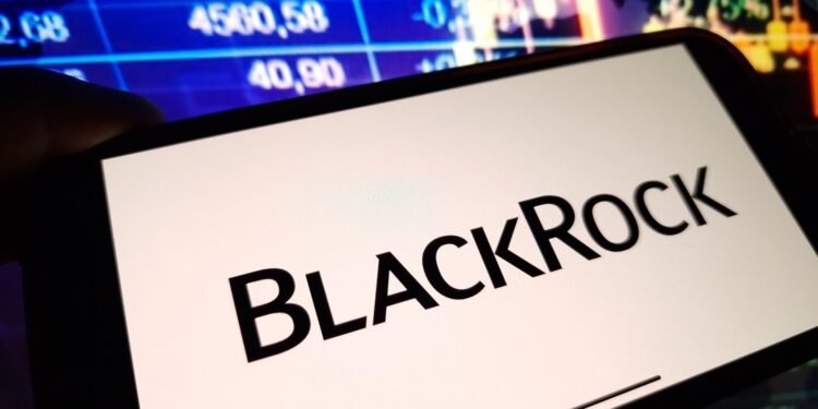 Un celular que muestra el logo de BlackRock delante de una pantalla de precios.