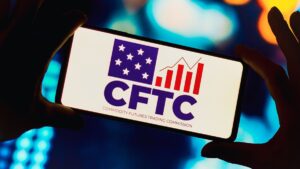 Par de manos sujetando un teléfono que refleja el logo de la CFTC.