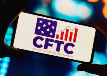 Par de manos sujetando un teléfono que refleja el logo de la CFTC.